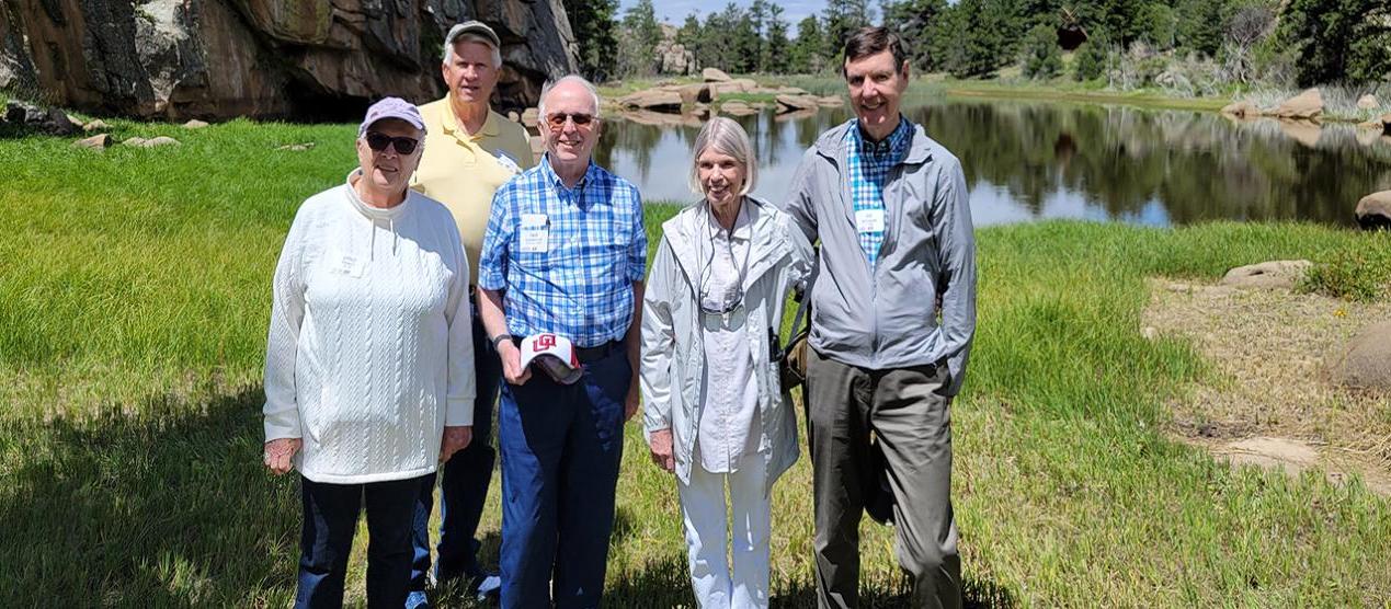 group of five older men and women standing in front of mountain lake